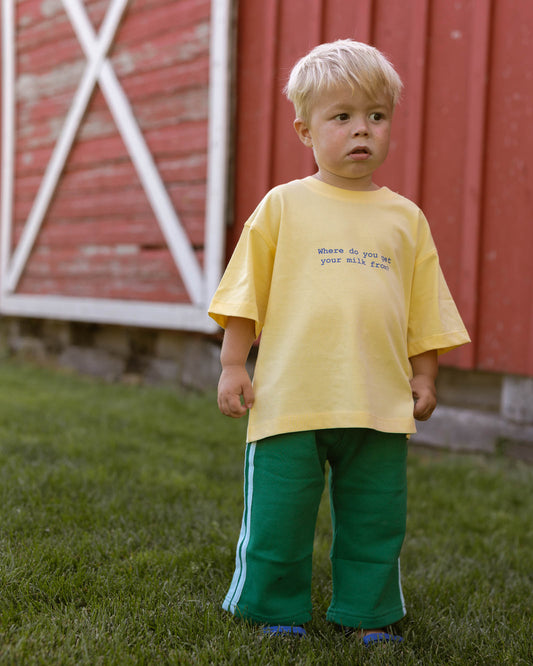 kid wearing a yellow t-shirt with blue text and green pants with blue side stripes.