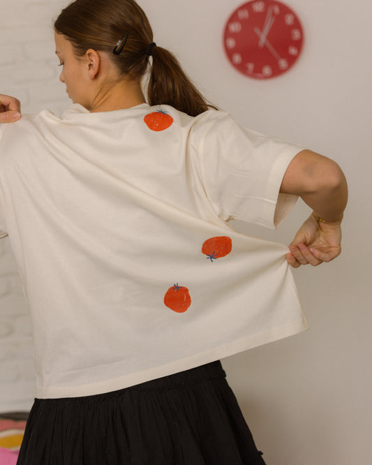 Person wearing a white shirt with tomatoes drawings, standing against a plain background.