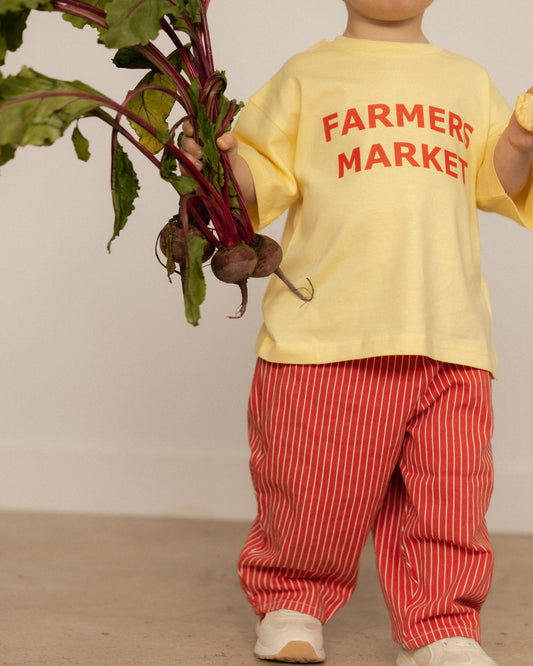 Child wearing a yellow shirt with 'Farmers Market' text, holding beets.