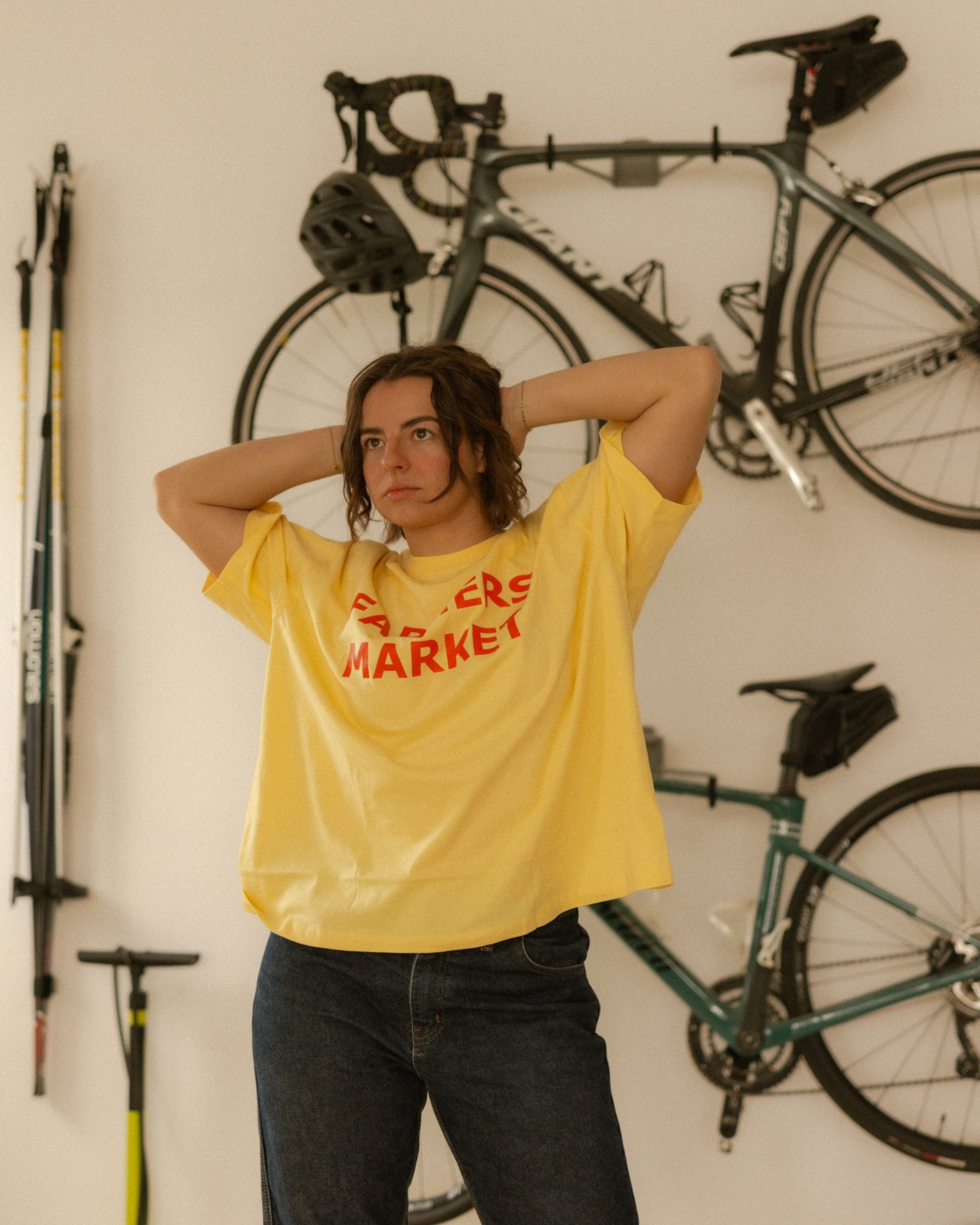 Person wearing a yellow t-shirt with red text in a room with bicycles on the wall