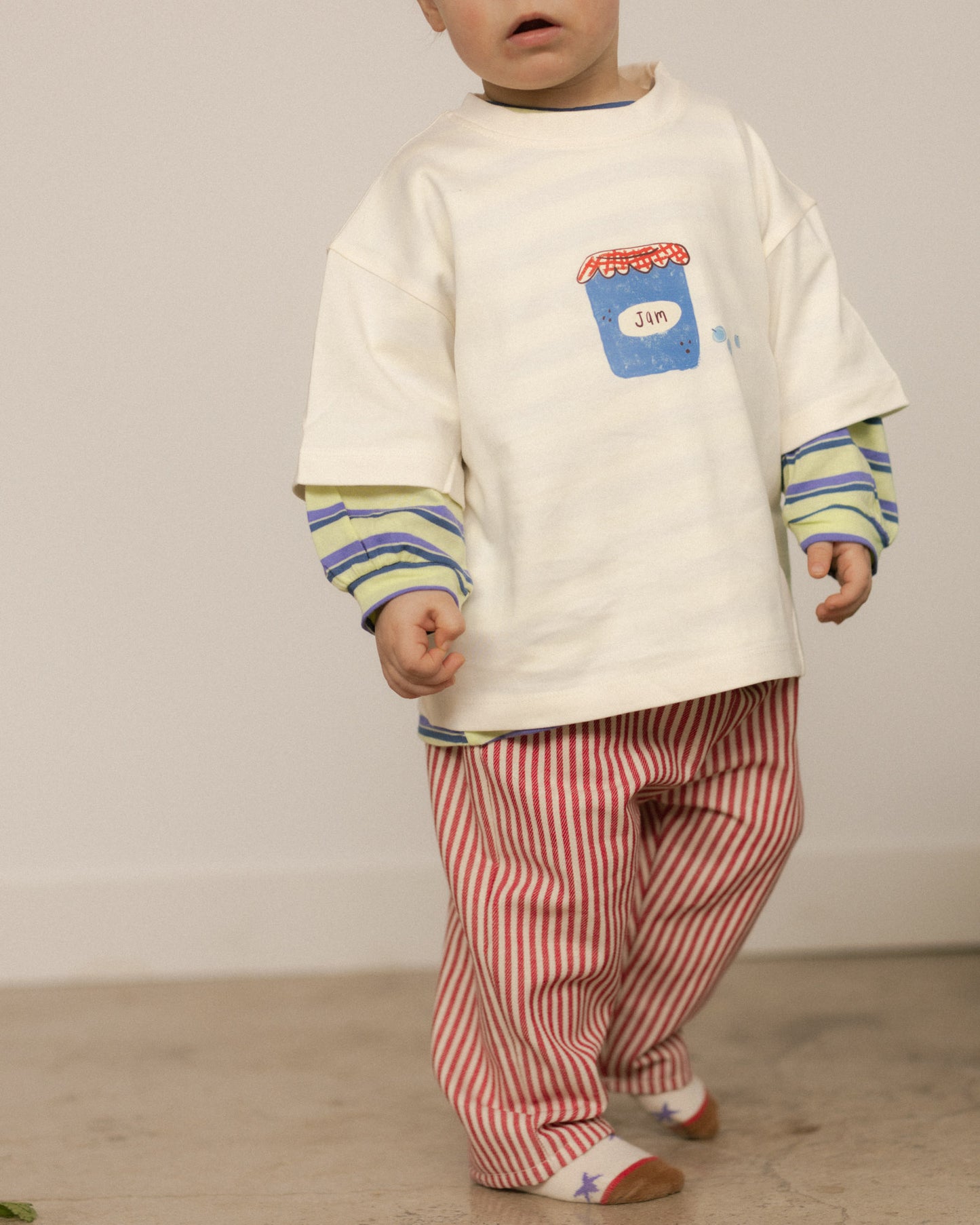 Child wearing a white graphic shirt with striped sleeves and red striped pants on a plain background
