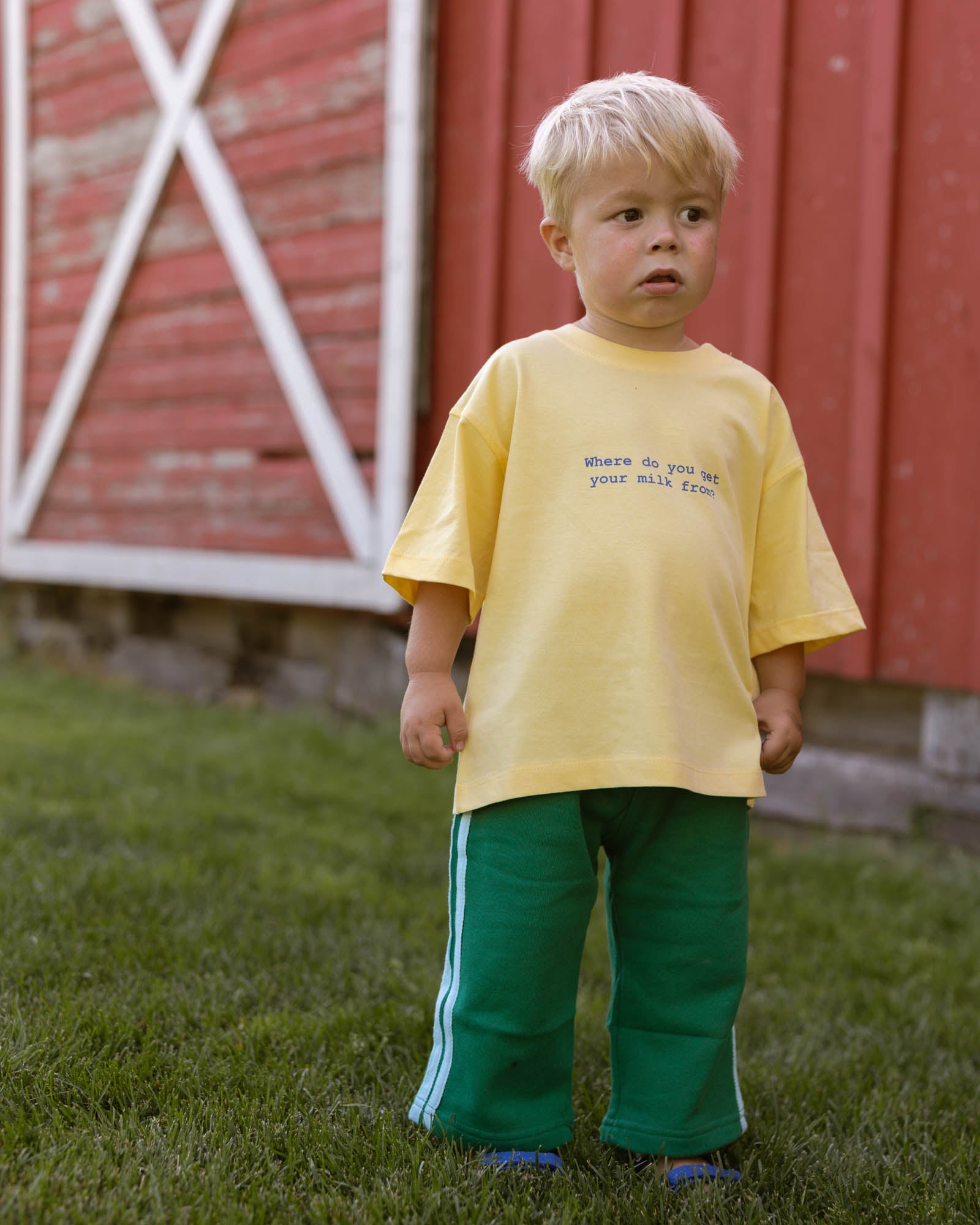 kid wearing a yellow t-shirt with blue text and green pants with blue side stripes.
