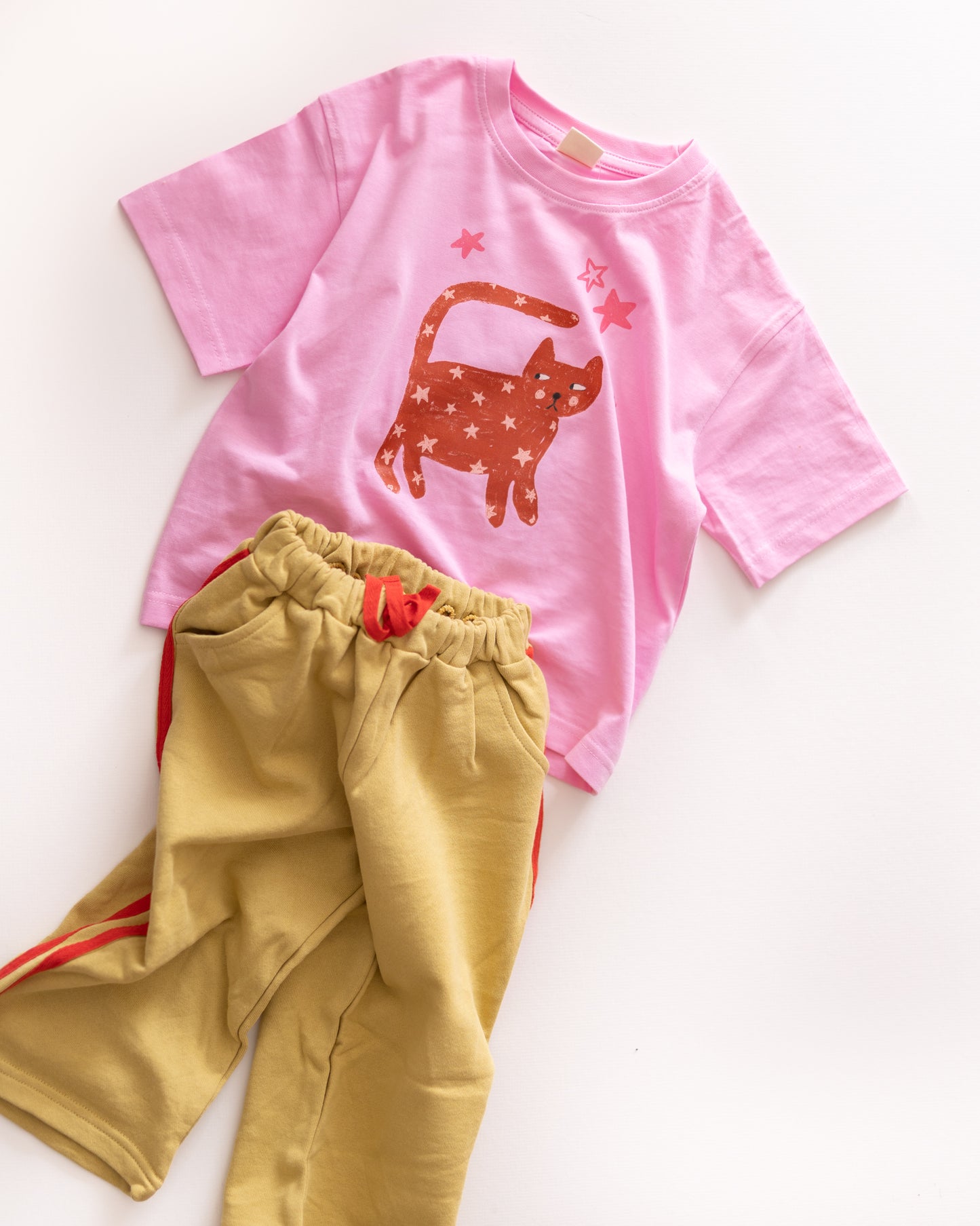 Pink t-shirt with a cat design and yellow pants on a white background