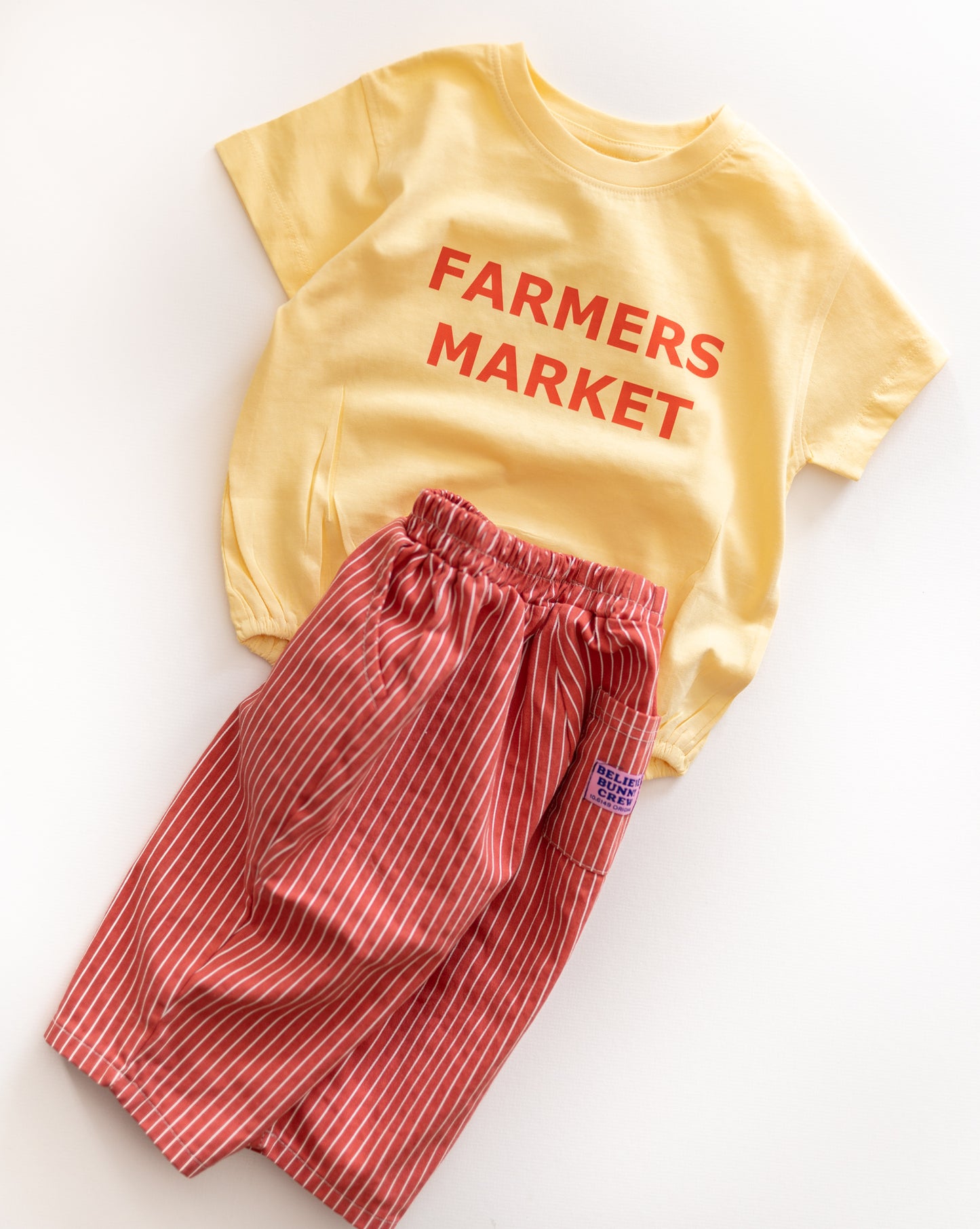 Yellow romper with 'Farmers Market' text and red striped pants on a white background
