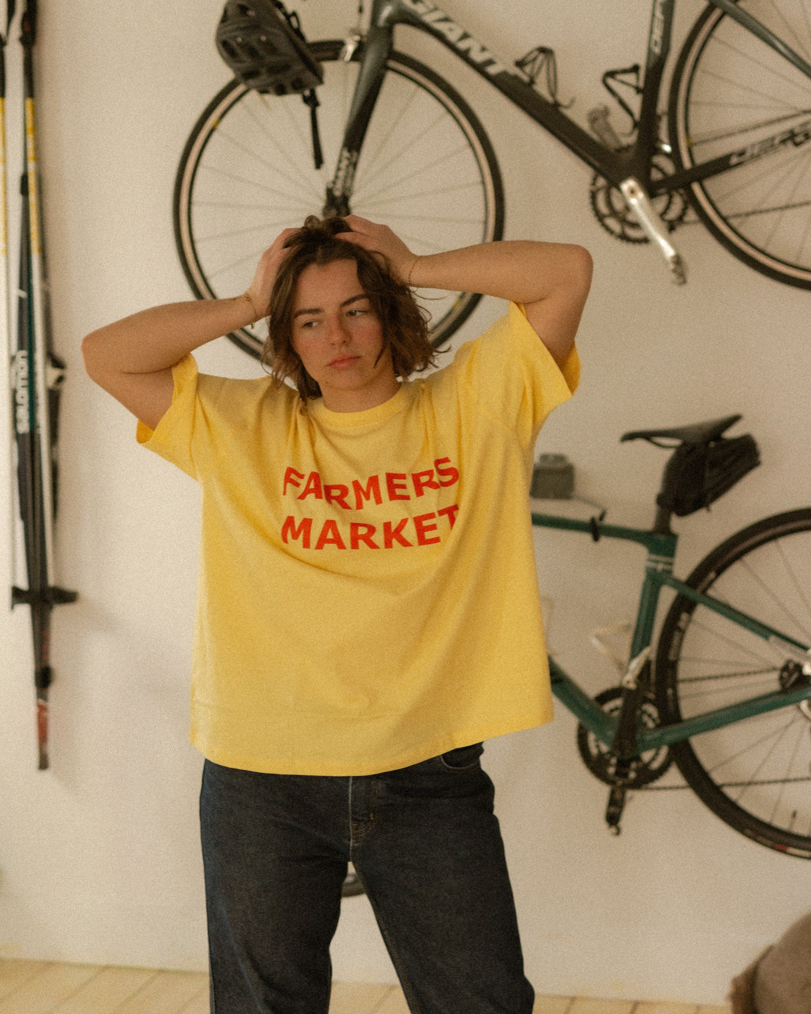 Person wearing a yellow 'Farmers Market' t-shirt with bicycles in the background.