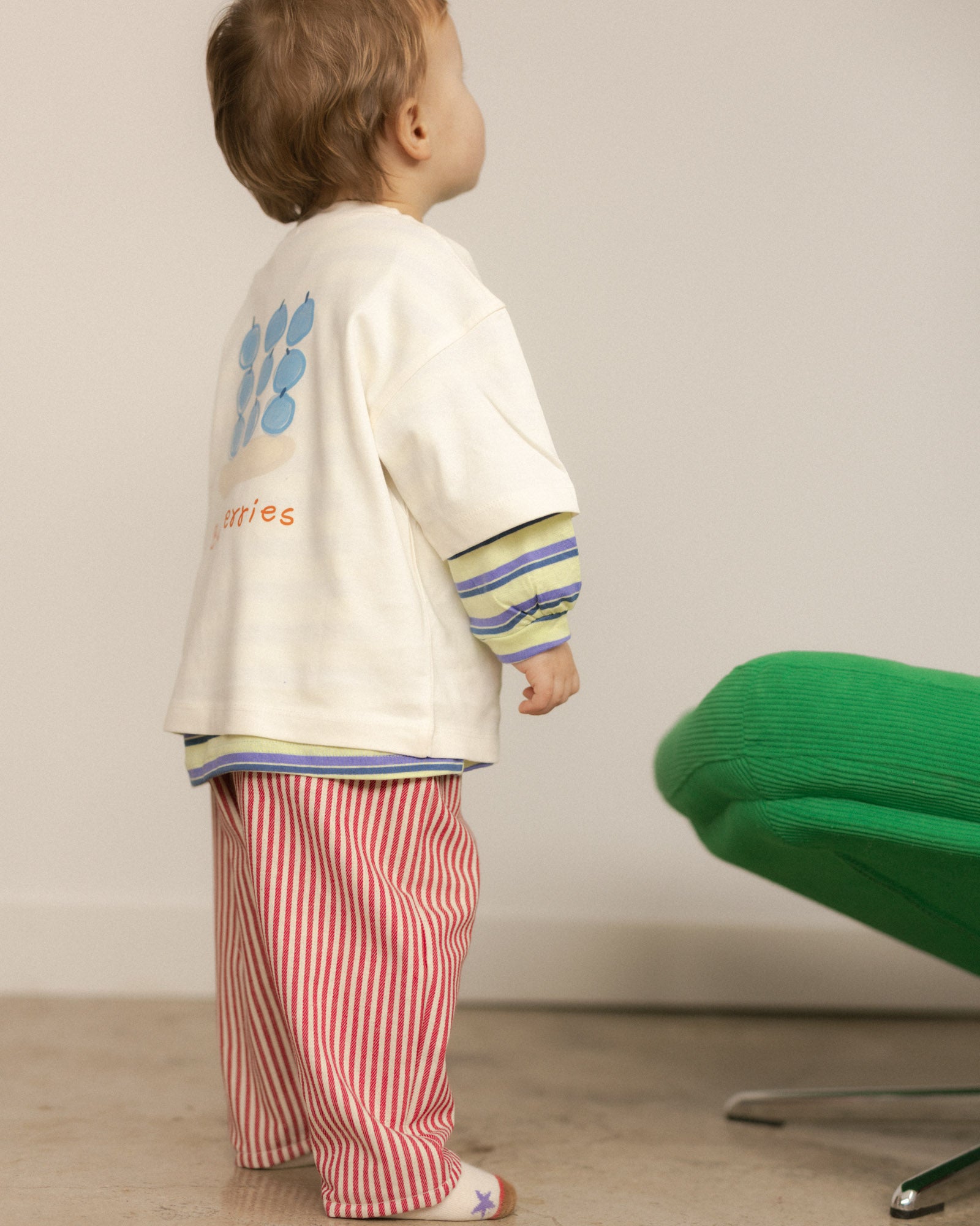 Child wearing a colorful outfit with a white graphic tee and red striped pants,