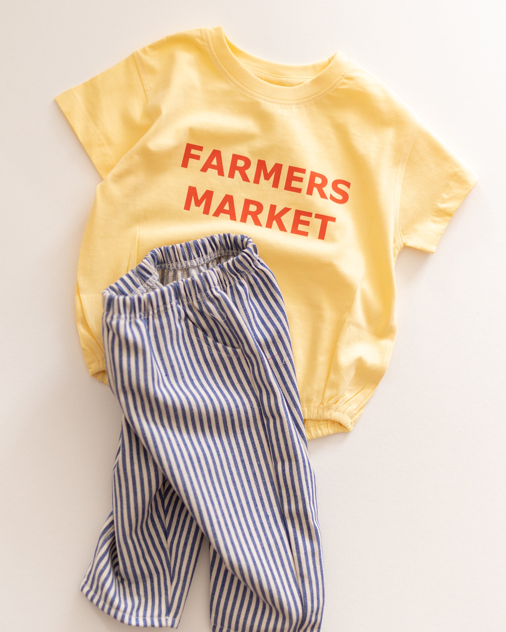 Yellow romper with 'Farmers Market' text and blue striped pants on a light background