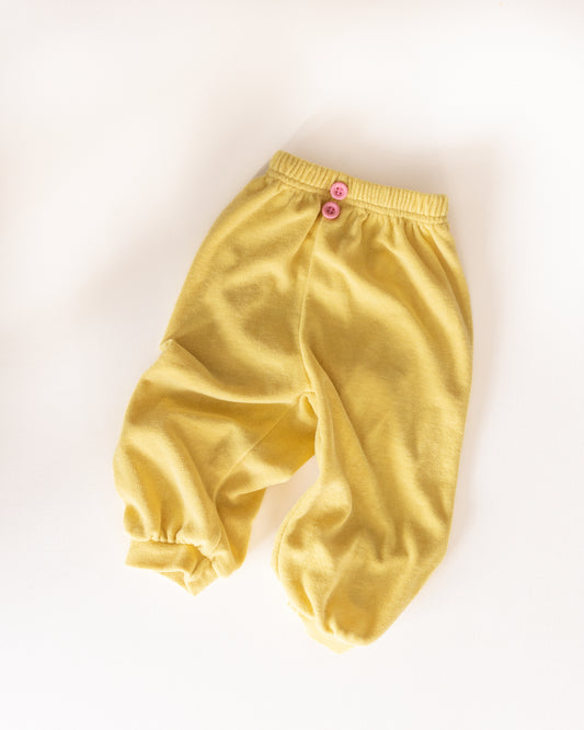 Yellow kids pants with pink buttons on a white background