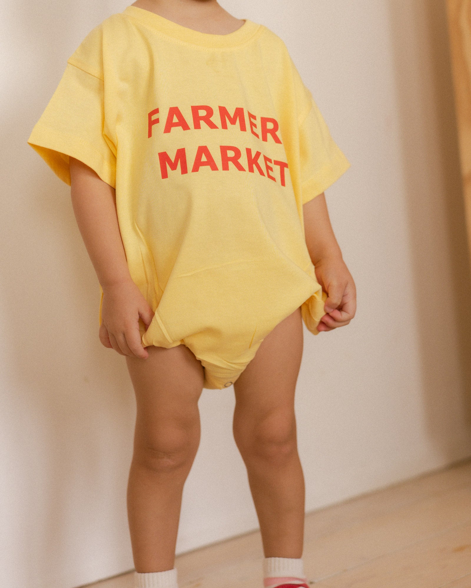 Child wearing a yellow 'Farmer Market' romper against a plain background