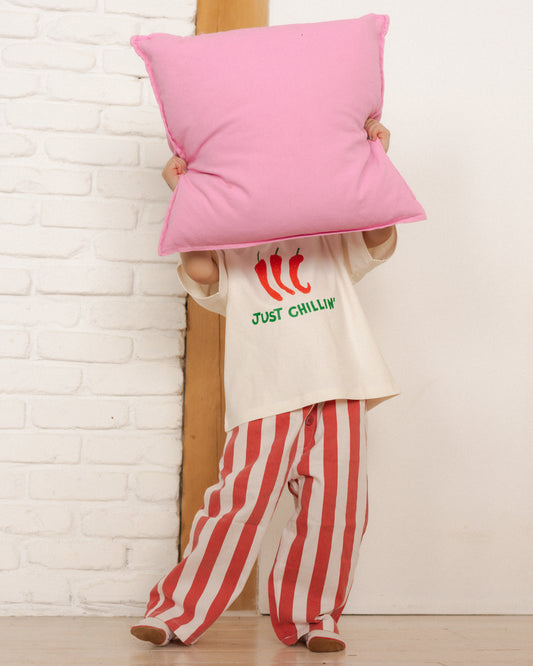kid wearing a 'Just Chillin'' shirt and red and white striped pants, holding a pink pillow.