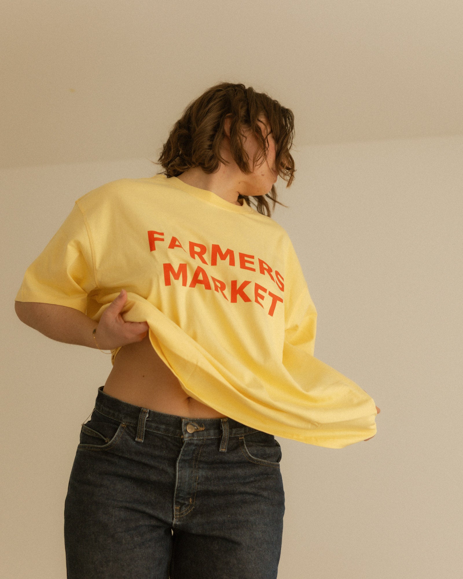 woman wearing a yellow 'Farmers Market' t-shirt against a plain background