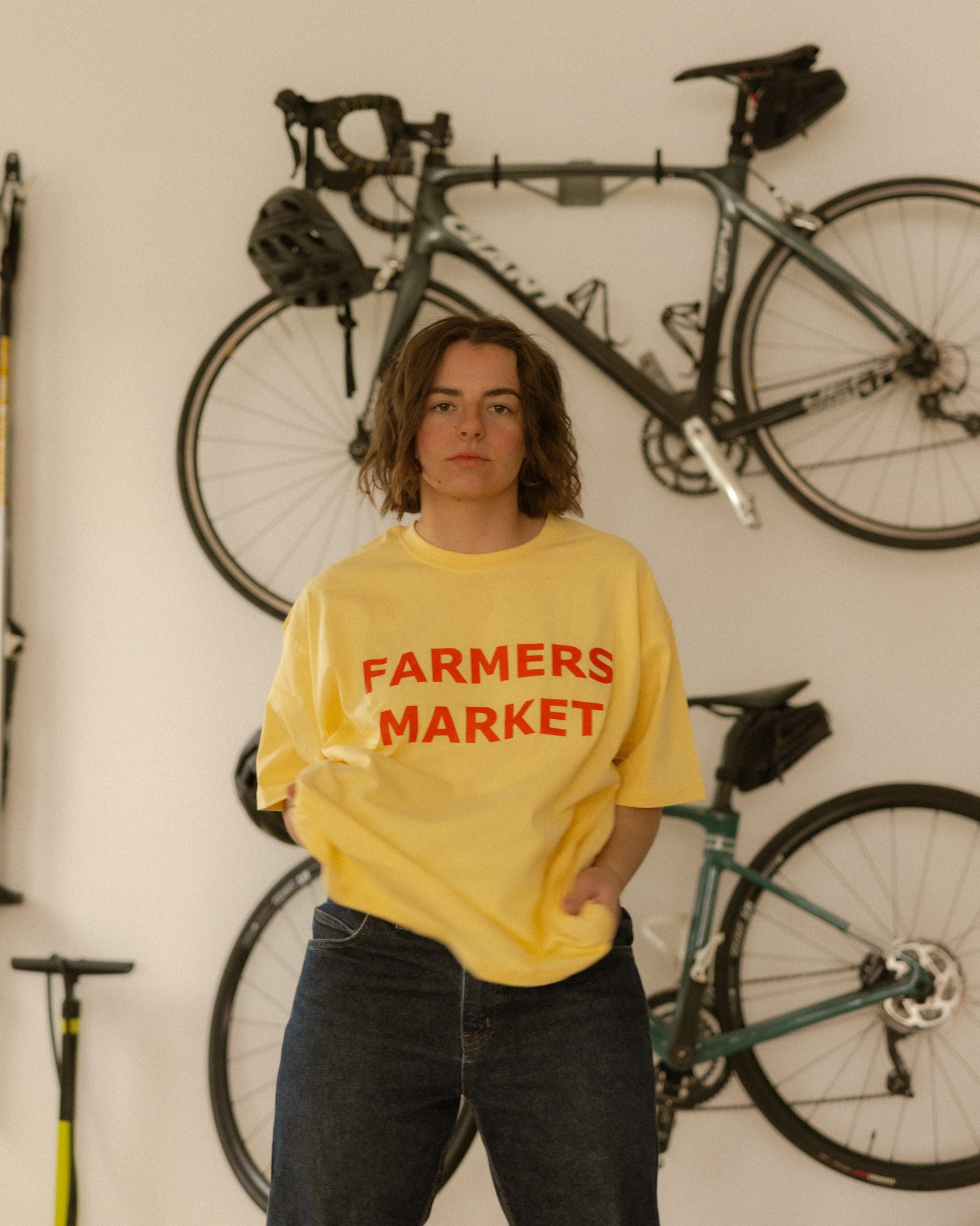 Person wearing a yellow 'Farmers Market' shirt standing in front of bicycles.
